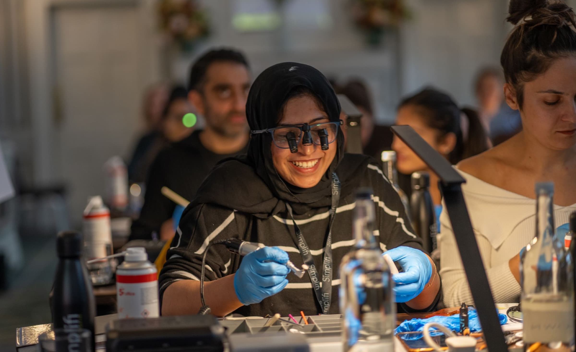 A delegate smiling in her loupes as she works at the bench on a Simplifi Composite course